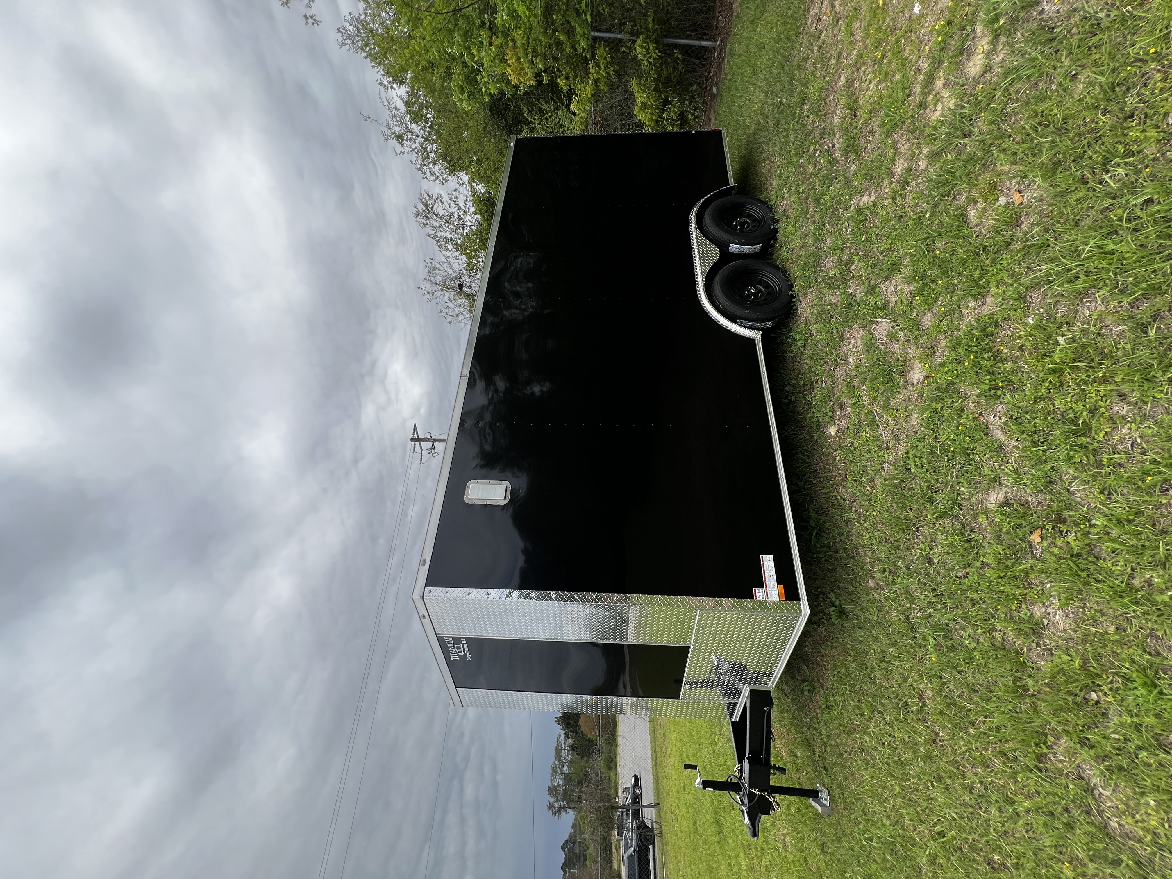 Black enclosed 8.5x16 tandem axle car hauler trailer with chrome trim and 6-inch mainframe — parked in grass lot