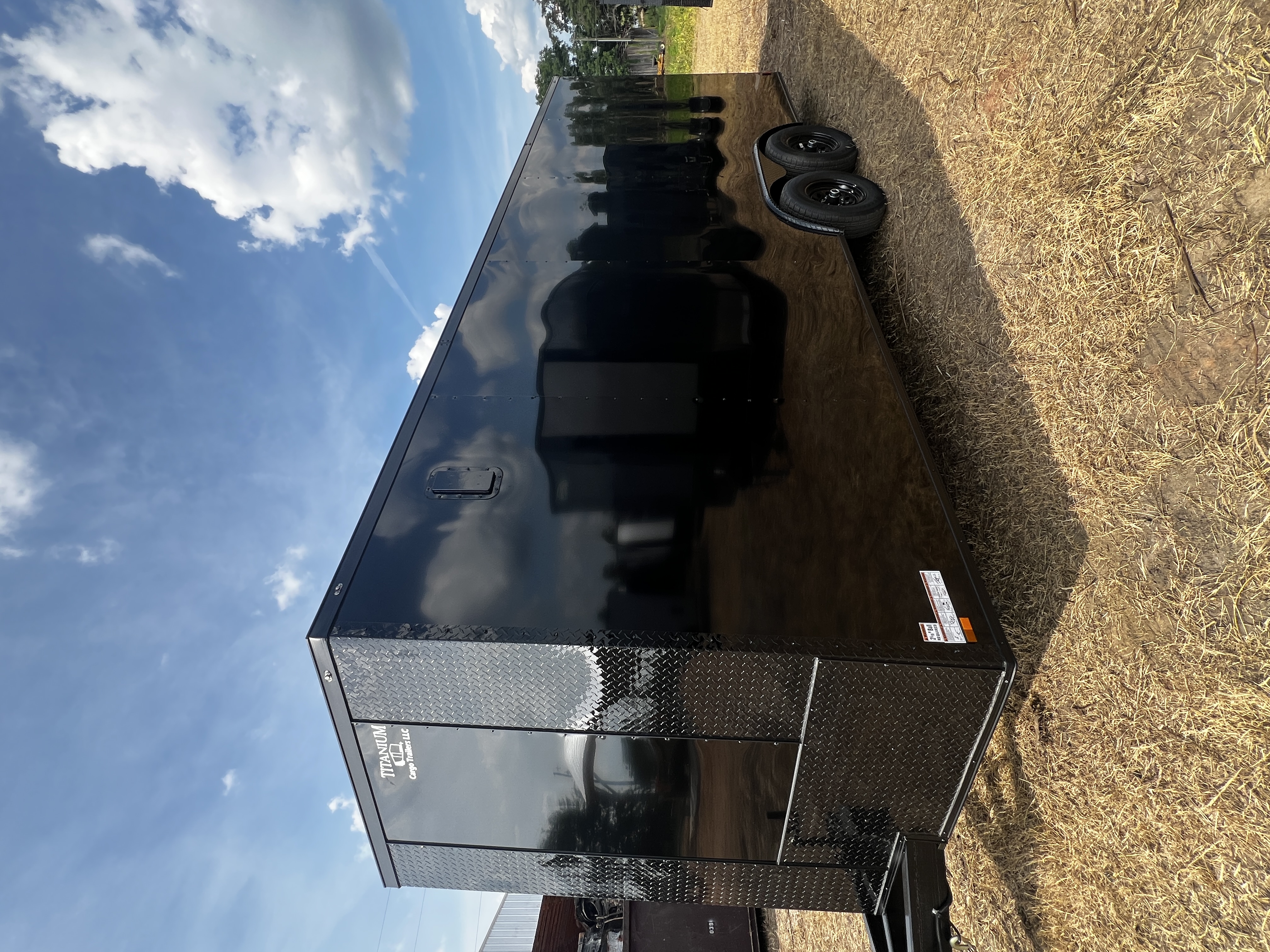 Black enclosed 8.5x24 tandem axle car hauler trailer with full blackout trim and triple-tube tongue — parked in dirt lot