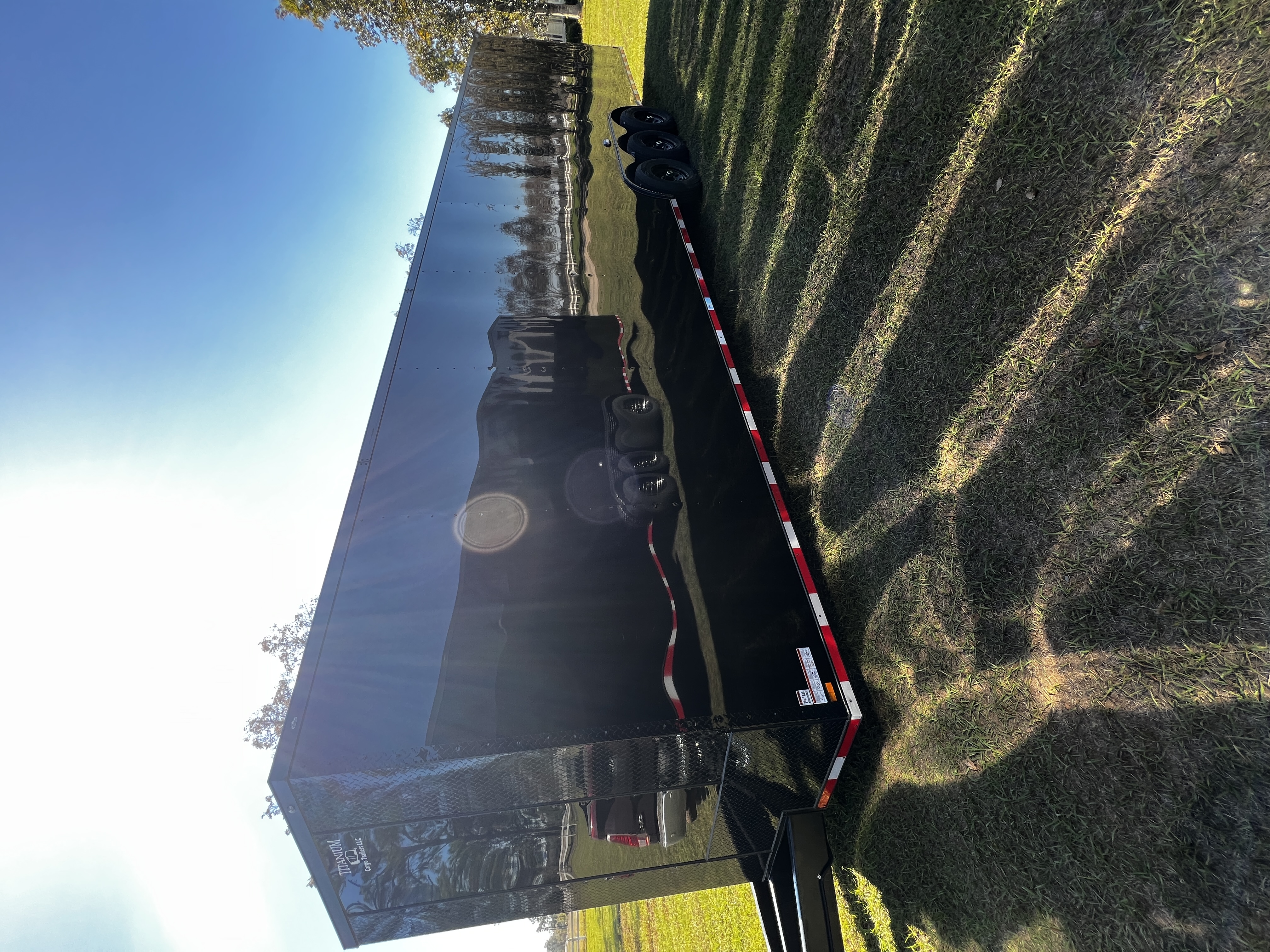 Black enclosed 8.5x36 triple-axle two-car hauler race trailer with blackout trim — parked in grass, featuring fully finished white metal interior