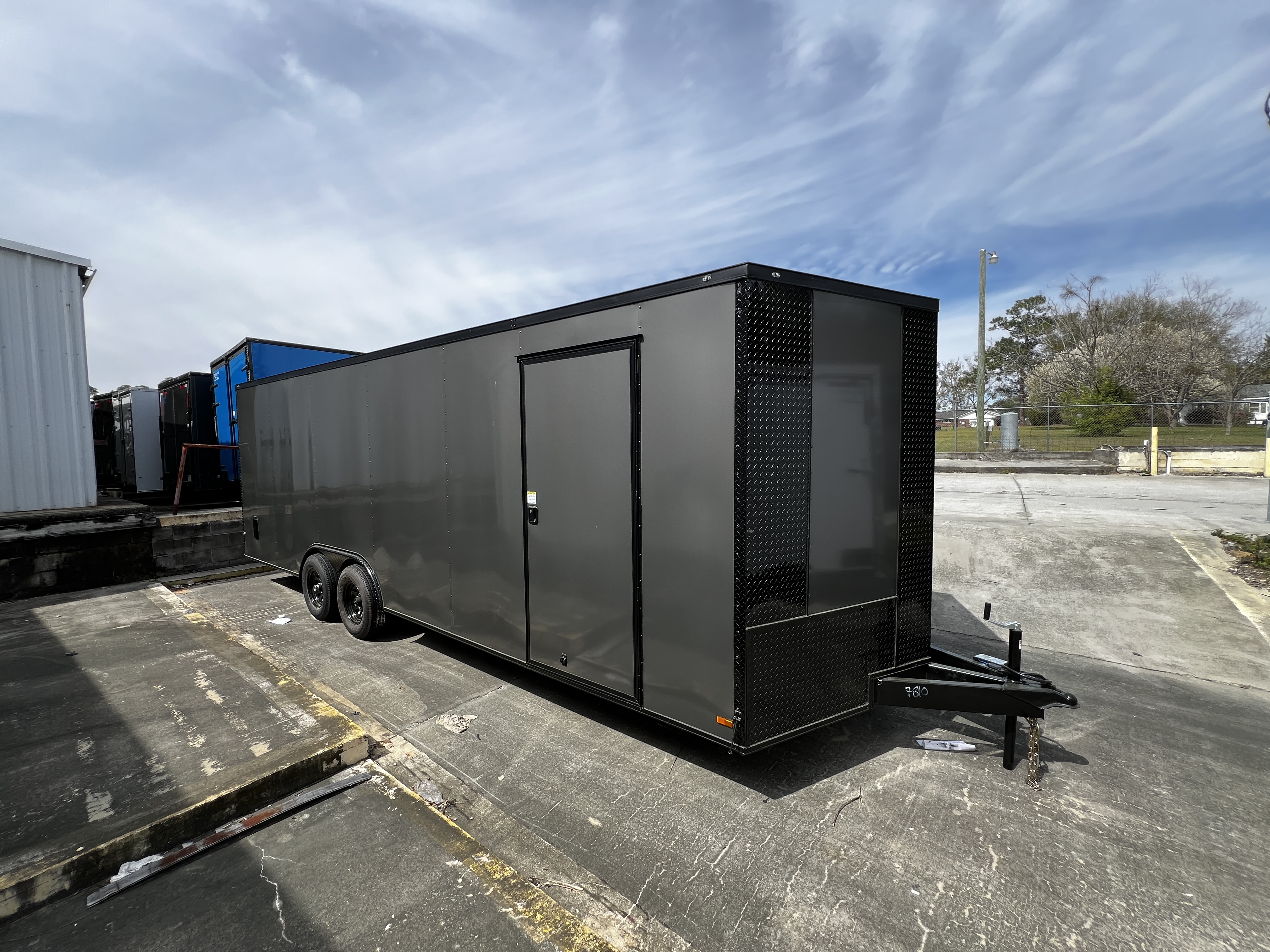 Charcoal grey Polycore enclosed 8.5x24 tandem axle car hauler trailer with blackout trim parked outdoors