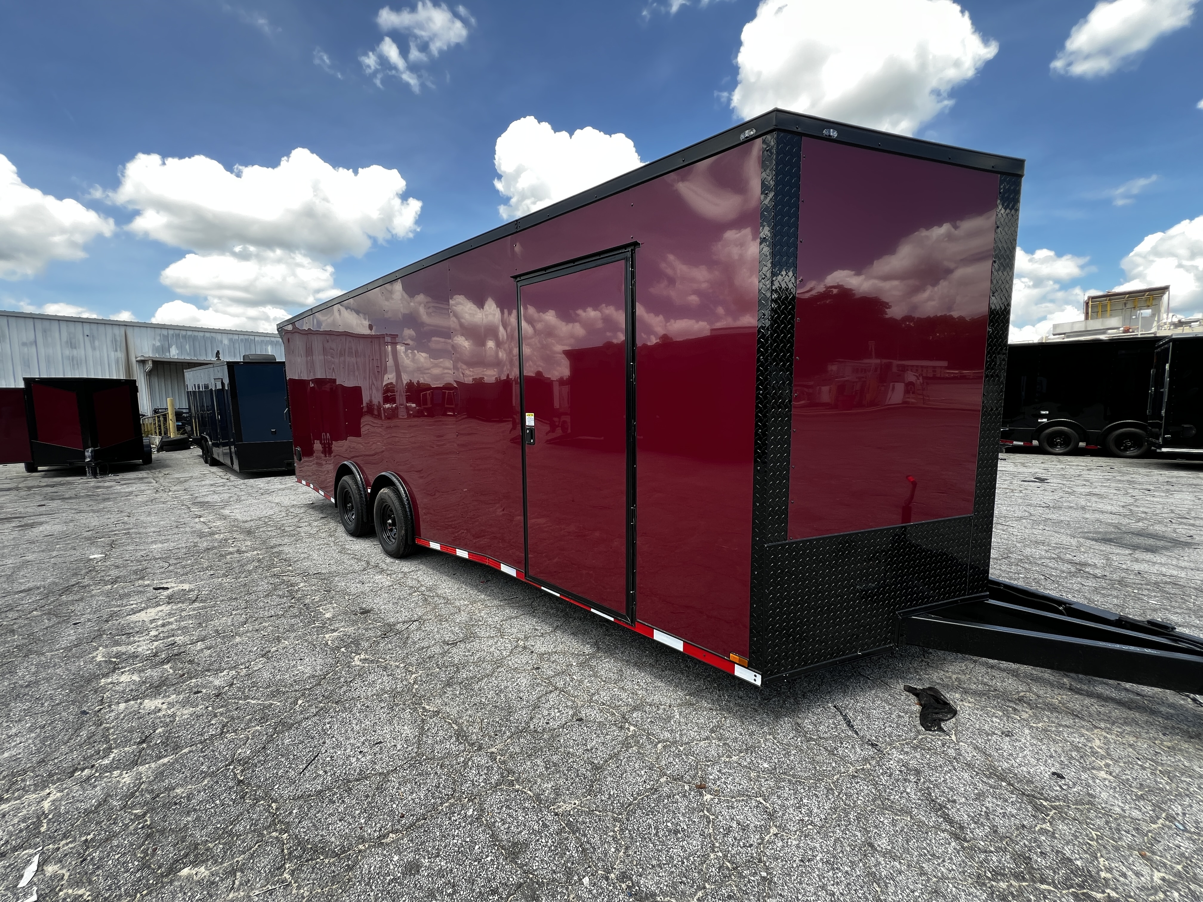 Brandy Wine (deep maroon) enclosed 8.5x24 tandem axle blackout car hauler — driver-side front view showing the slanted V-nose with black ATP diamond-plate trim, blackout fenders and wheels, and side man door