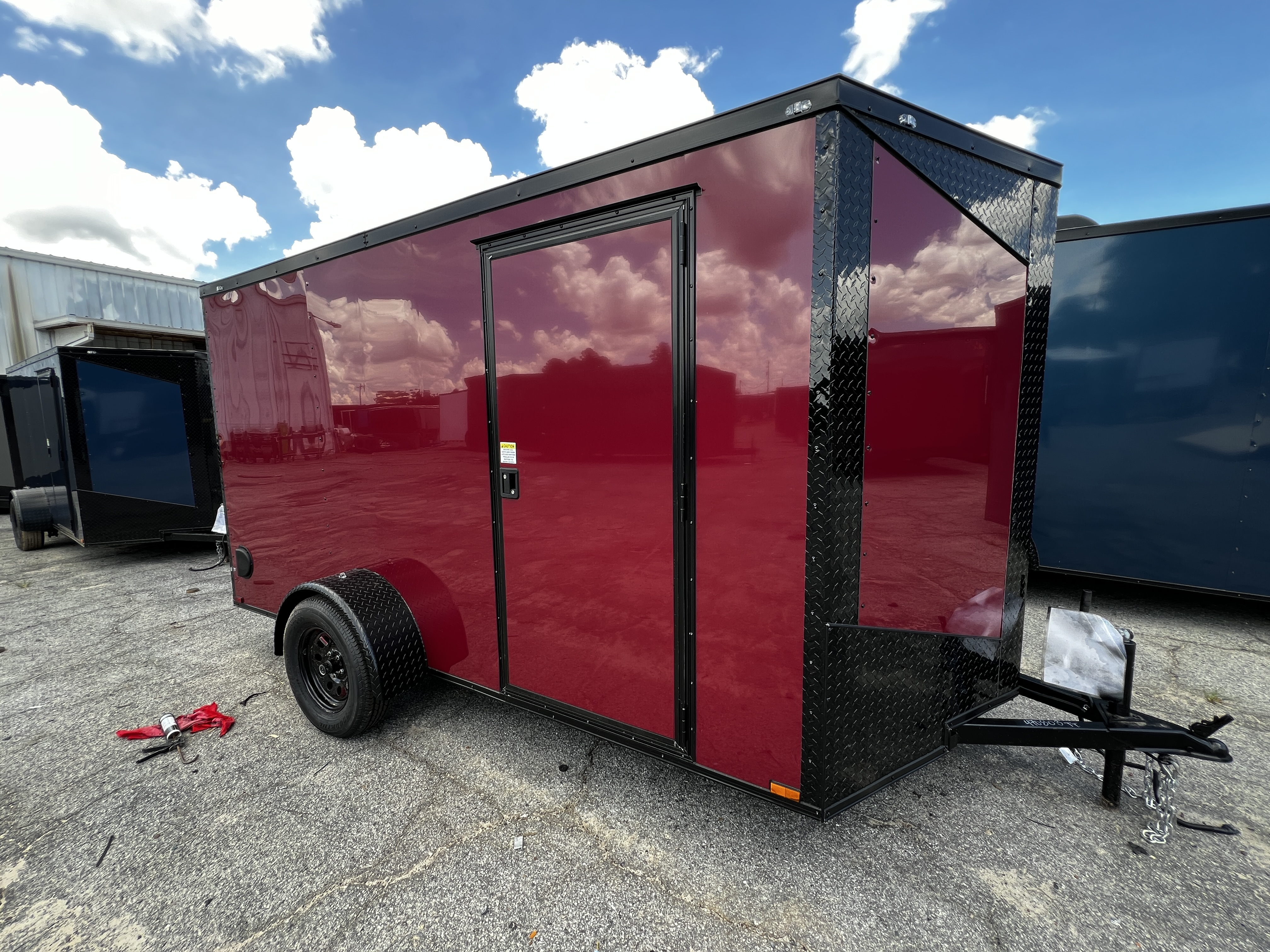 Brandy Wine (deep maroon) enclosed 6x12 single axle cargo trailer — front driver-side view showing the slanted V-nose with black ATP diamond-plate trim, blackout fender and wheel, and passenger-side man door