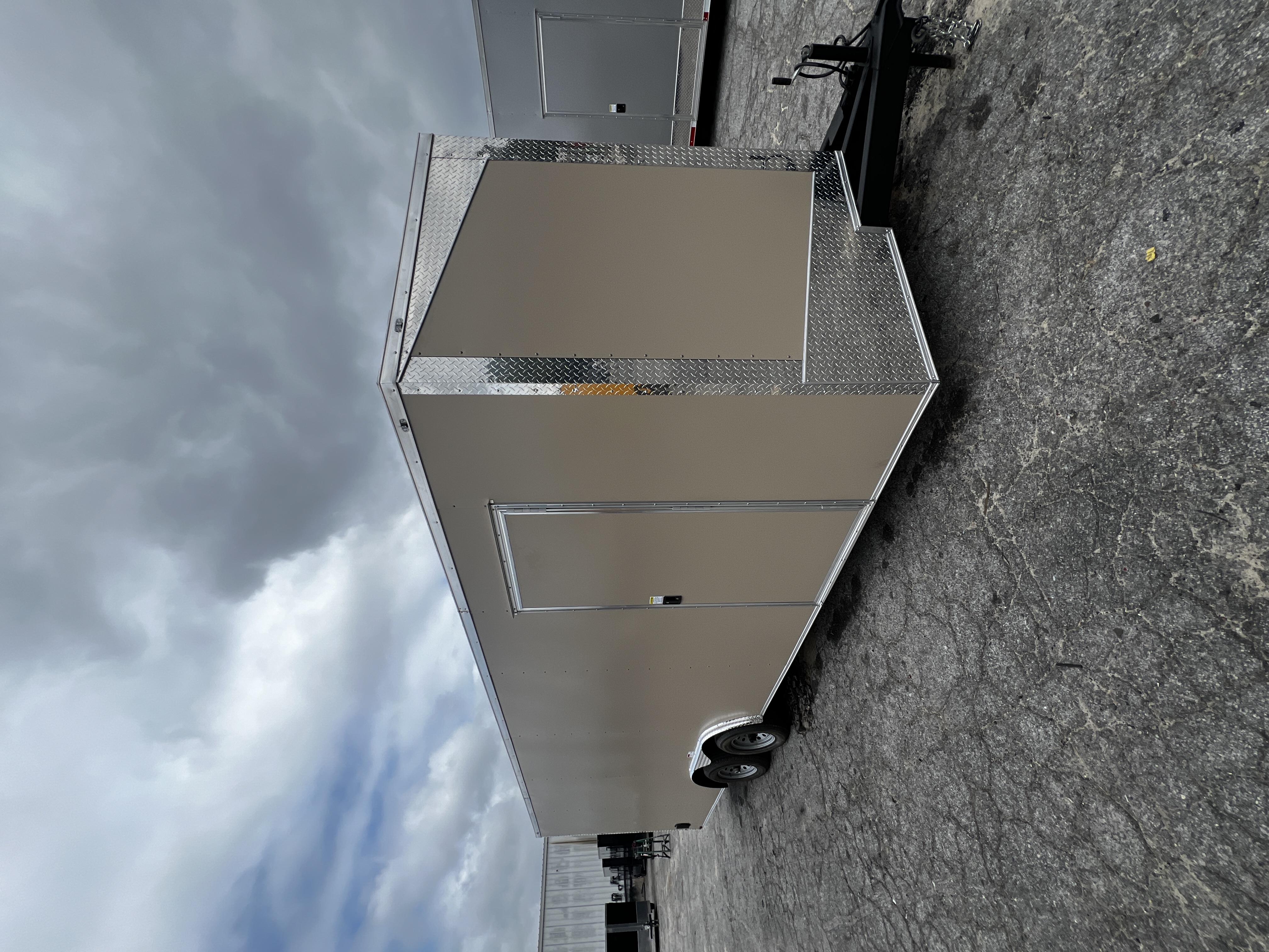Pewter (champagne/tan) enclosed 8.5x26 tandem axle car hauler — driver-side front view showing the slanted V-nose with polished chrome ATP diamond-plate trim, chrome stone guard, and curb-side man door
