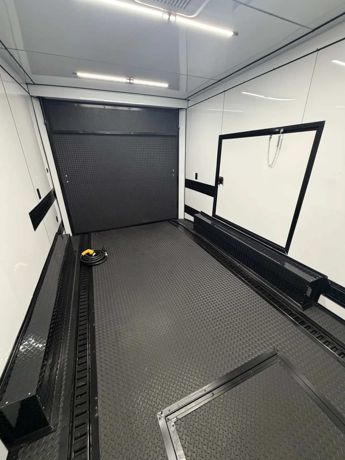 Rear-facing interior view with rubber tread plate flooring, recessed floor and wall E-track, white metal walls and ceiling, escape door, and closed ramp