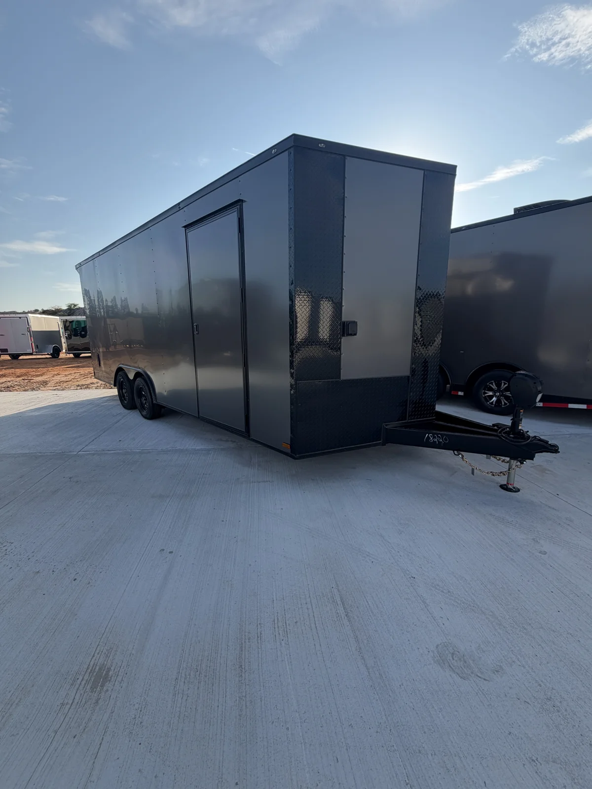 Charcoal Grey 8.5x20 tandem-axle Blackout race trailer in an outdoor concrete lot, front passenger-side view showing black nose, side door, and electric jack