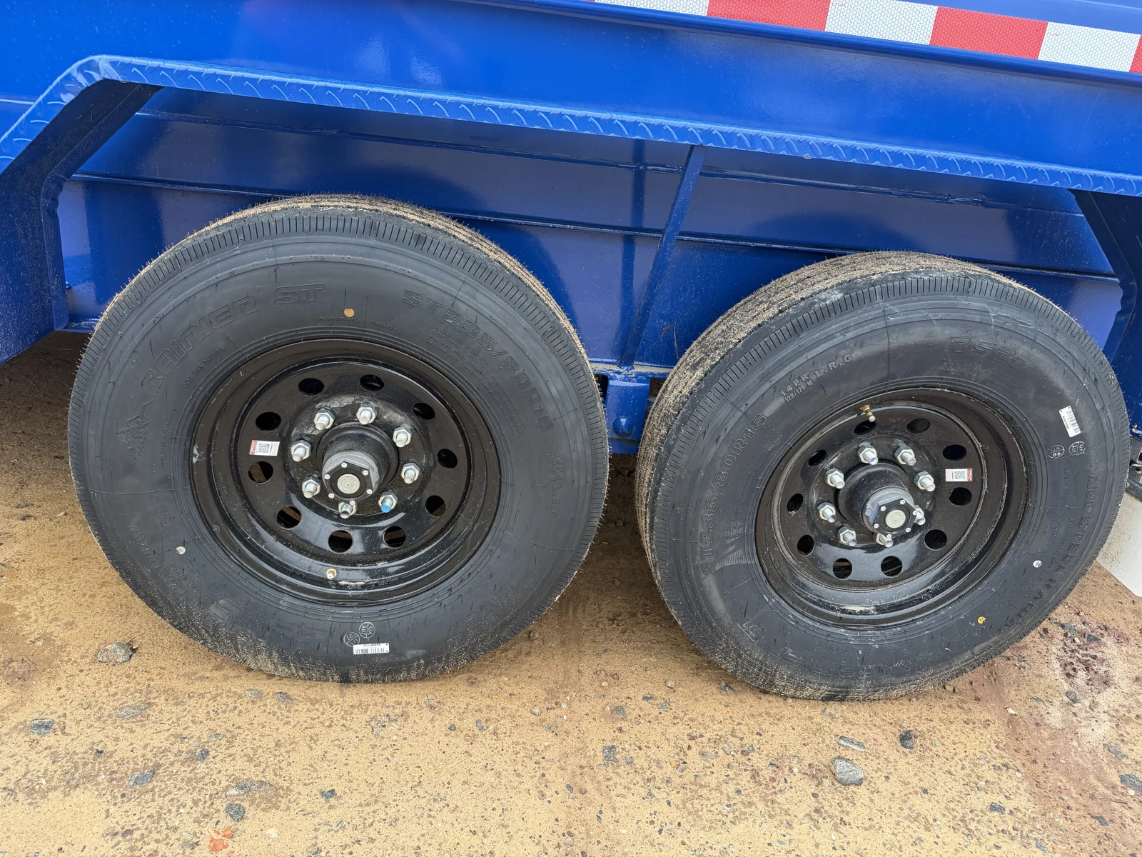 Close-up of the dump trailer tandem tires and black steel wheels under a Royal Blue fender