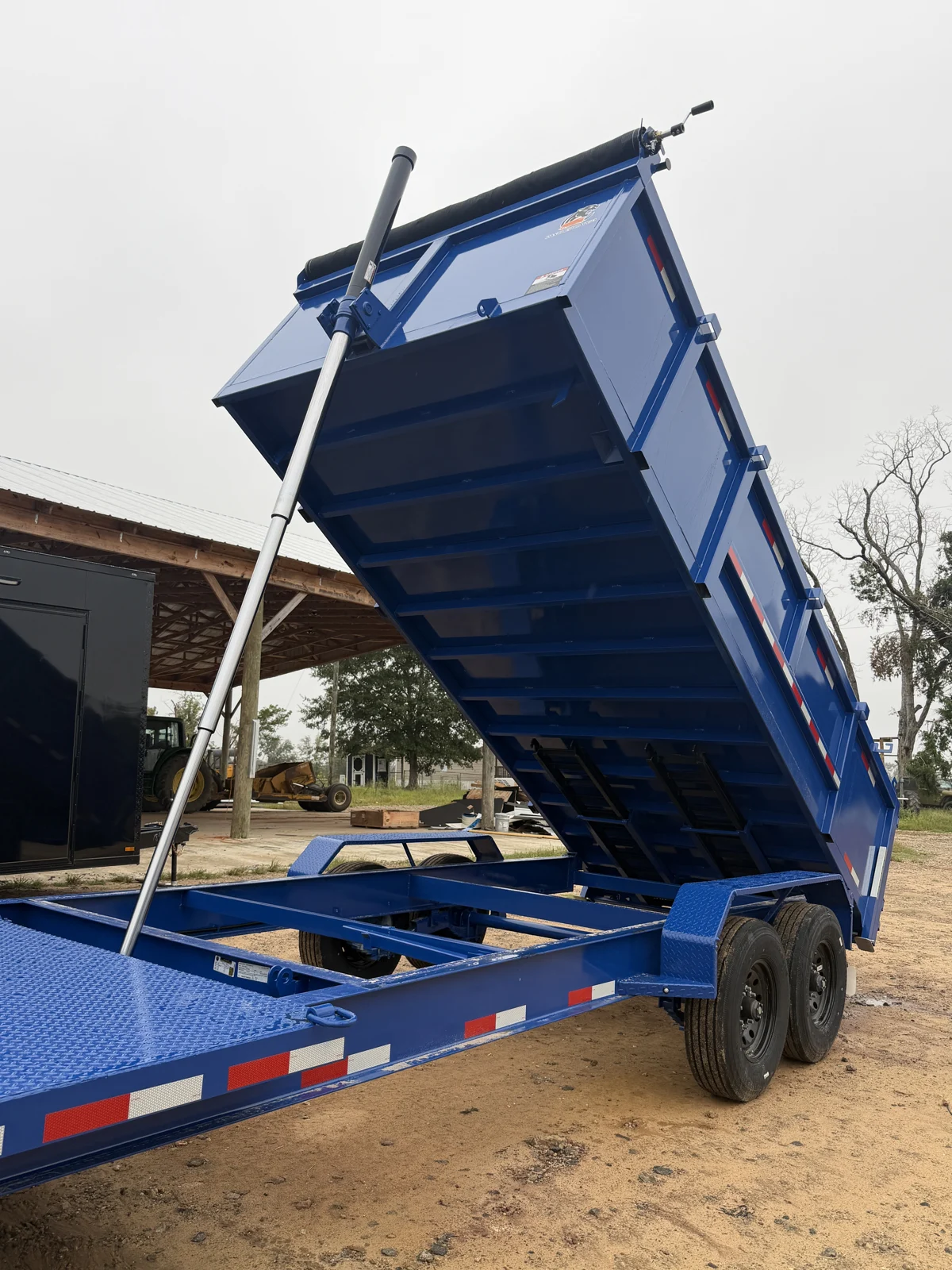 Royal Blue dump box raised by a single hydraulic cylinder, showing the underside, frame, tandem wheels, and rolled tarp