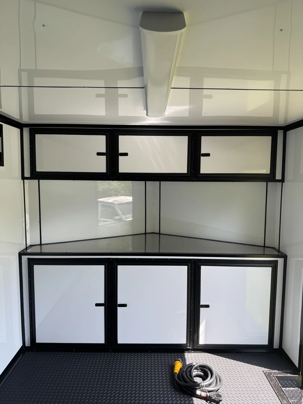 White base and overhead cabinets with black trim at the front of the race trailer, with a ceiling bar light and coiled power cord