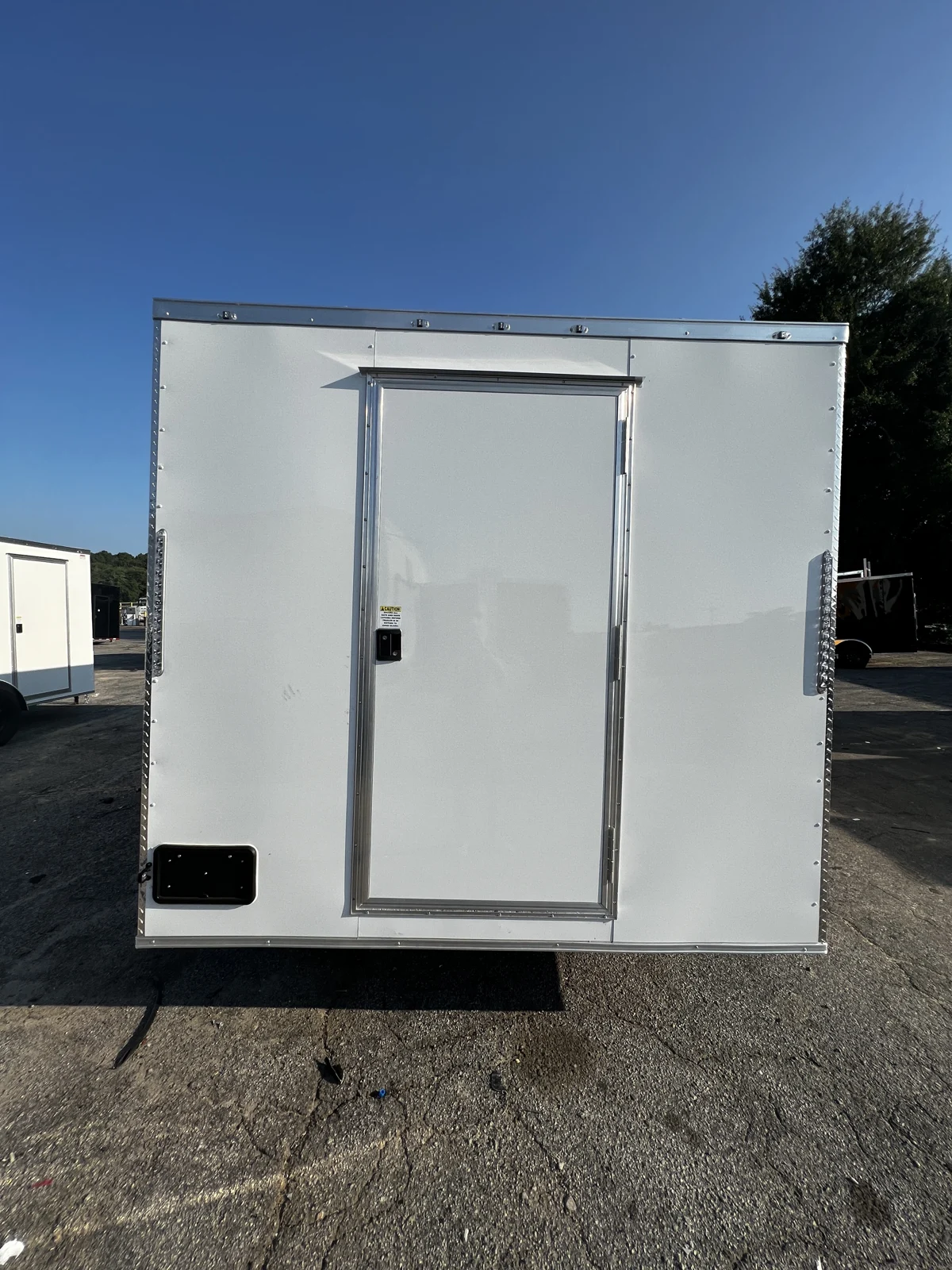 White rear wall of the 8.5x16 concession trailer with a centered entry door and silver trim on a paved lot