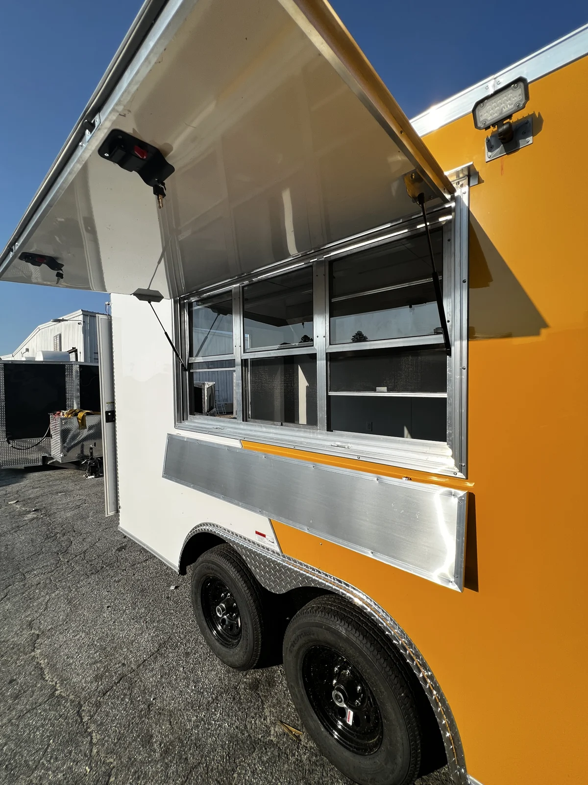 Open concession window with glass and screen, exterior serving shelf, and window light above the tandem wheels