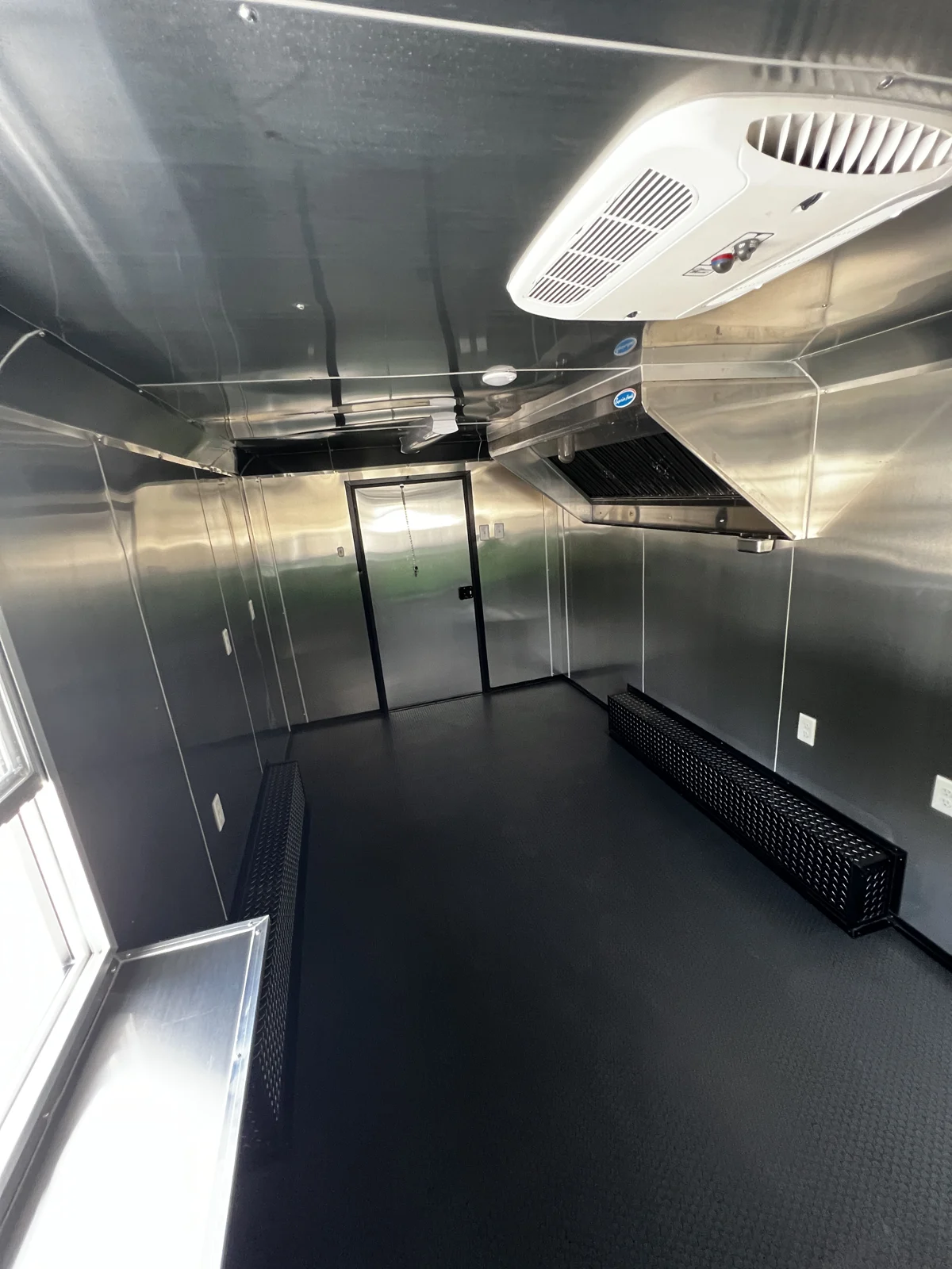 Concession trailer interior looking toward the entry door, showing mill-finish lining, hood vent, and open equipment floor space