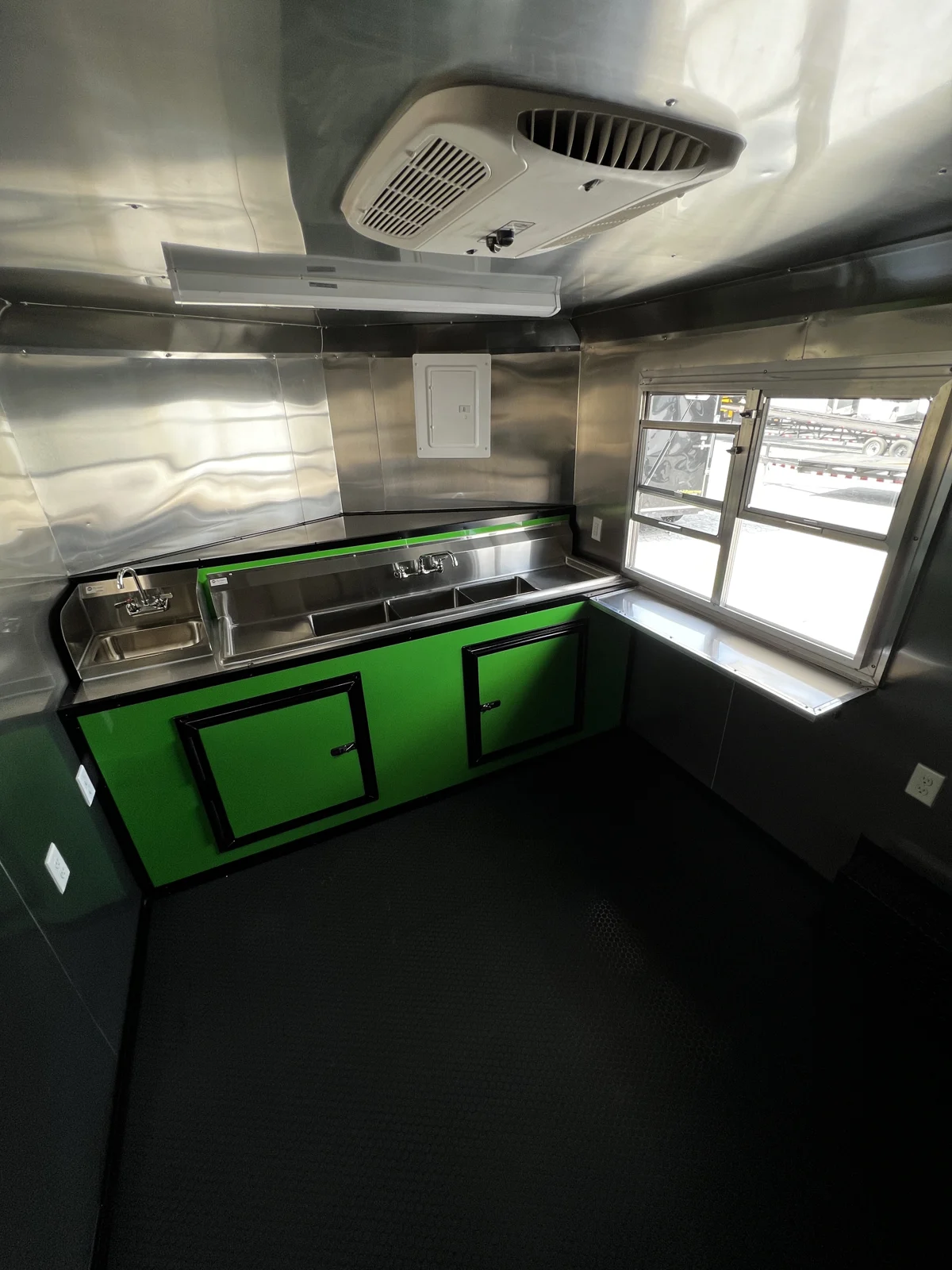 Concession trailer water setup with sinks, green base cabinets, countertop work area, and service window