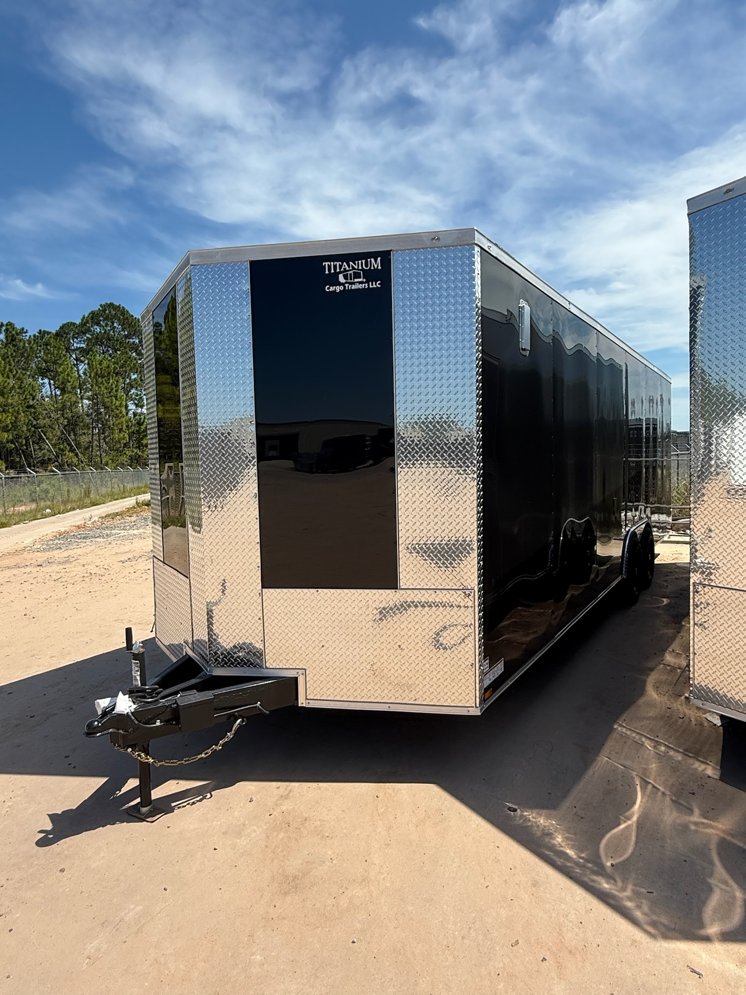 Black enclosed 8.5x24 tandem axle car hauler trailer — front driver-side view showing the slanted V-nose, polished chrome ATP diamond-plate front cap and stone guard, chrome trim, black wheels, and side man door on an outdoor trailer lot